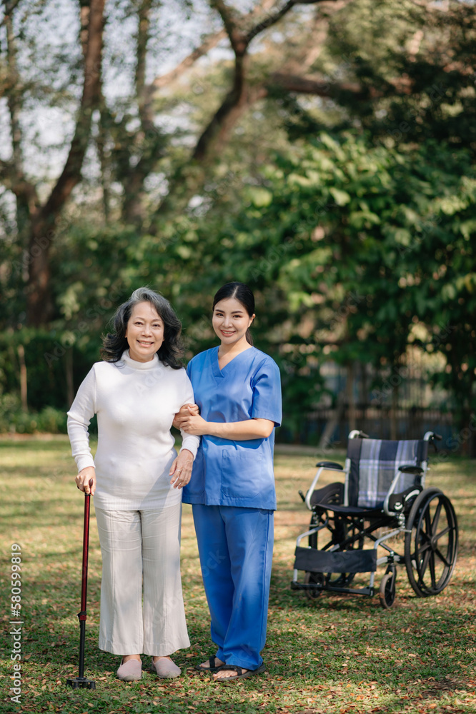 Asian careful caregiver or nurse and the happy patient in a wheelchair are walking in the garden to help and encourage and rest your mind with green nature. Help support yourself Asian careful caregiver or nurse and the happy patient in a wheelchair are walking in the garden to help and encourage and rest your mind with green nature. Help support yourself