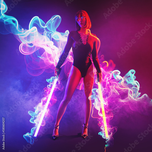 Neon full body futuristic young woman in sunglasses with glow sticks as a laser sword in the curvy neon light.