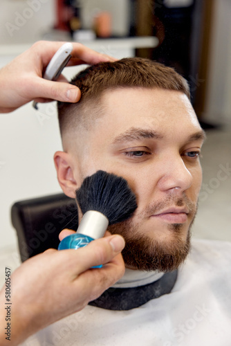 Hairstylist serving handsome man in barber shop.