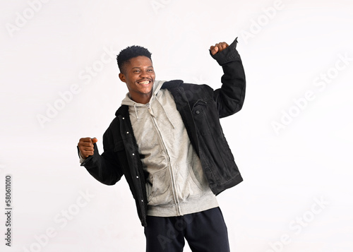 Photo of extremely happy overjoyed hipster man wearing grey hoodie and black denim jacket standing isolated over white background, rejoicing, celebrating, dancing with raised arms.