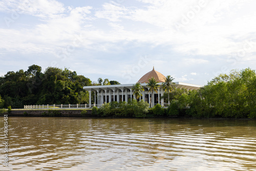  trees, boat and building along Sungai Kedayan river, the capital of Brunei Darussalam in sunny day with white coulds and blue sky