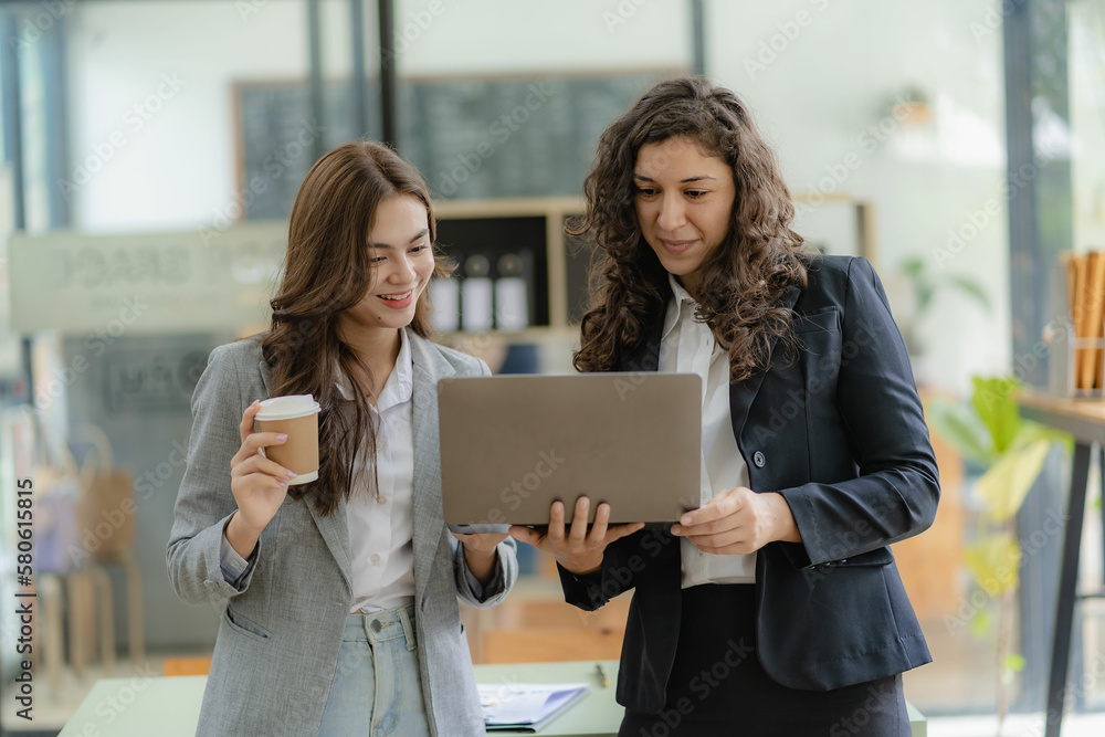 Two cheerful businesswoman working using laptop computer at conference table with work documents at office. Business colleagues for meeting to discuss real estate project Two cheerful businesswoman working using laptop computer at conference table with work documents at office. Business colleagues for meeting to discuss real estate project