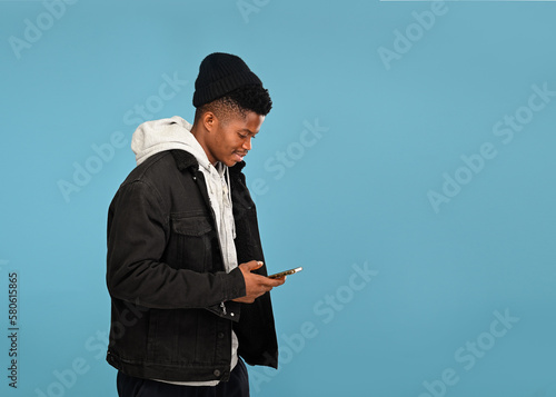 Side view of happy African man with Jacket smiling while using cellphone, chatting on social media, enjoying mobile service. empty copy space for advertisement, indoor studio shot