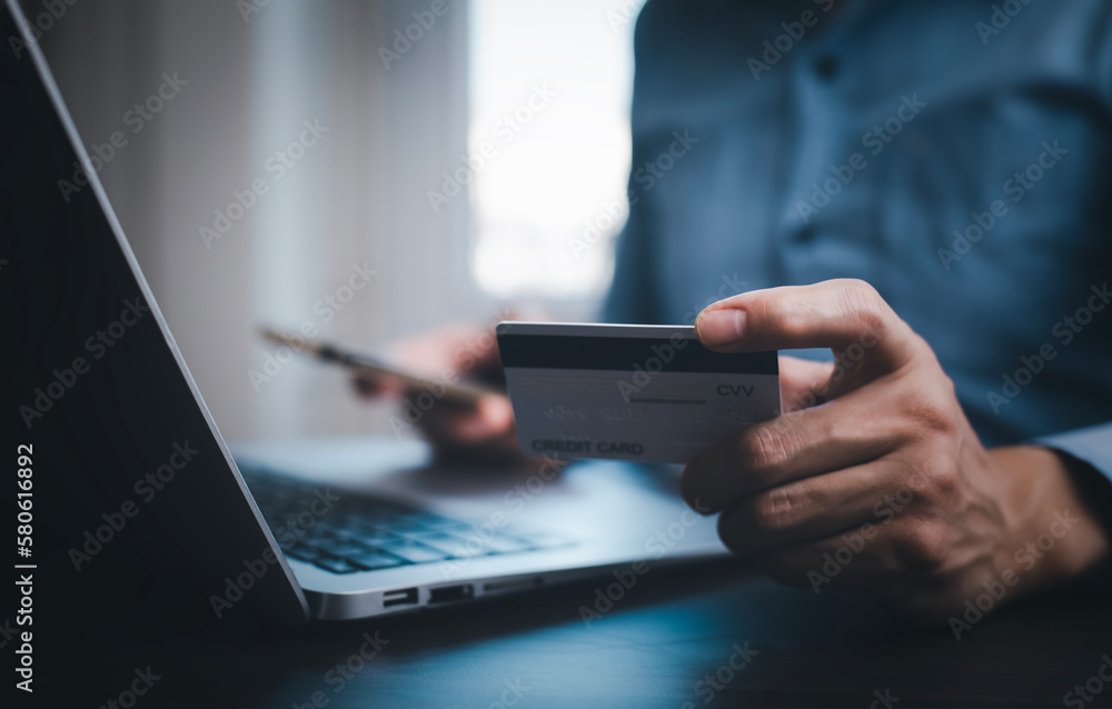 Hand holding credit card for makes a purchase on the Internet on the laptop computer with credit card, online payment, shopping online, e-commerce, internet banking, spending money concept. Hand holding credit card for makes a purchase on the Internet on the laptop computer with credit card, online payment, shopping online, e-commerce, internet banking, spending money concept.
