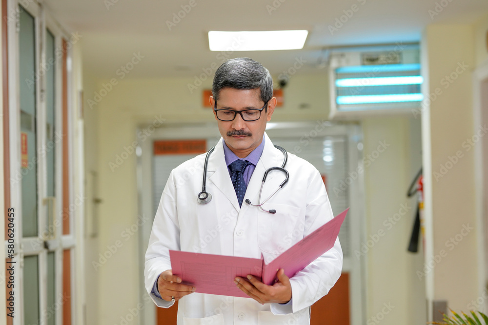 Indian senior doctor watching medical report at hospital.