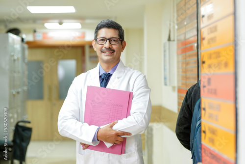 Indian male doctor holding file in hand and standing at hospital.