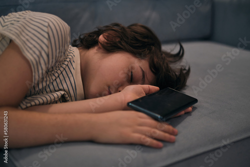child fell asleep with a cell phone in his arms, on the couch. the impact of gadgets on the emotional and psychological state of children. differences in sleep habits and how they can affect