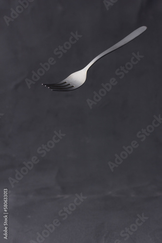 Matte fork suspended on dark textured background.