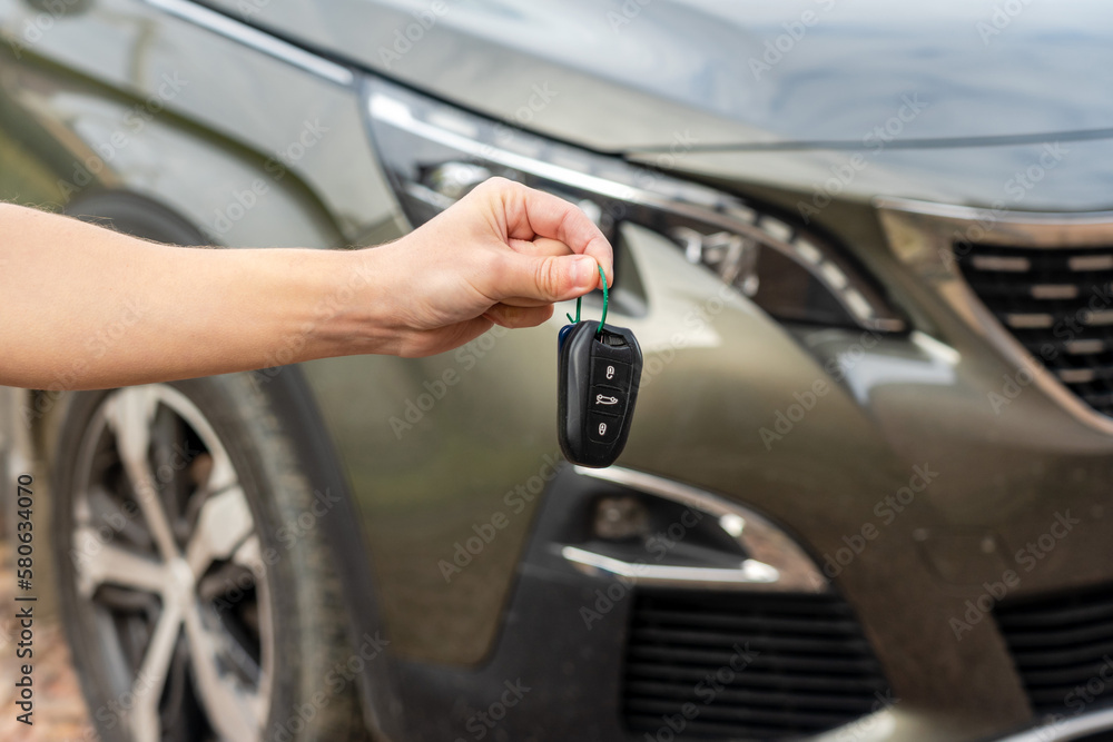 Person holding a car key in the hand stands front car. Insurance, loan and buying car concept