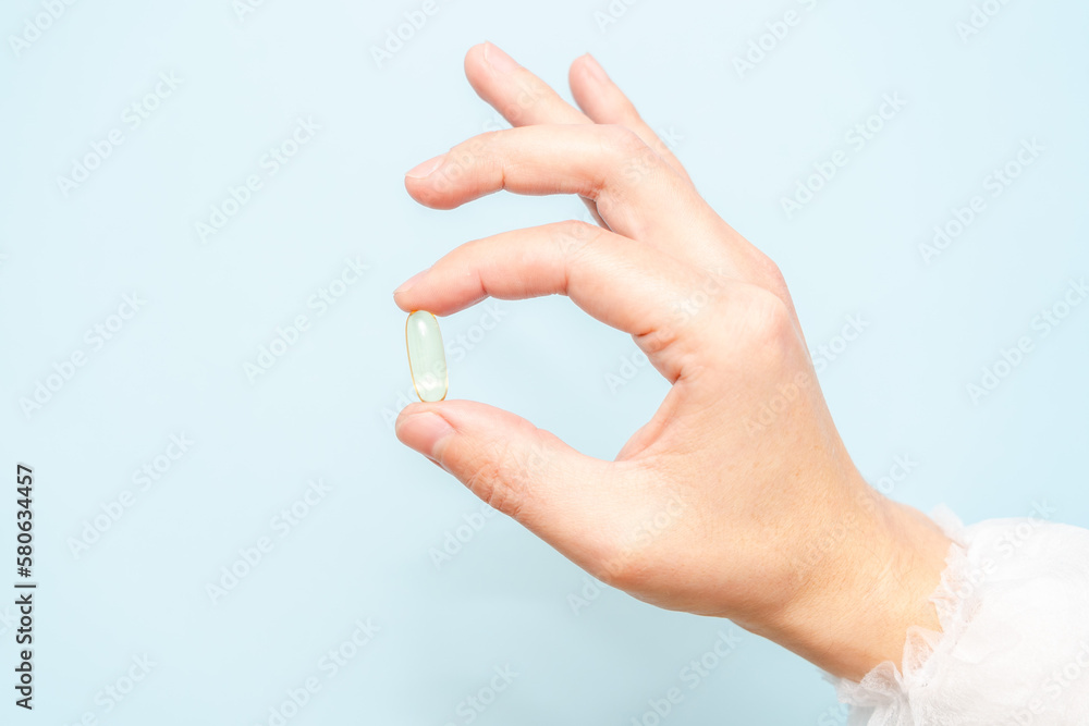 Doctor's hand holding a fish oil capsule (Omega 3) or pill isolated on light blue background Doctor's hand holding a fish oil capsule (Omega 3) or pill isolated on light blue background