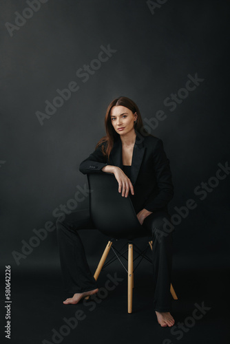 Portrait of a modern stylish woman. Beautiful brunette woman posing on a chair on a black background.