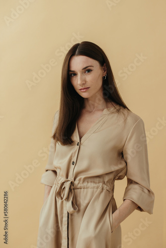 Portrait of a beautiful elegant brunette in a long dress on a beige background.