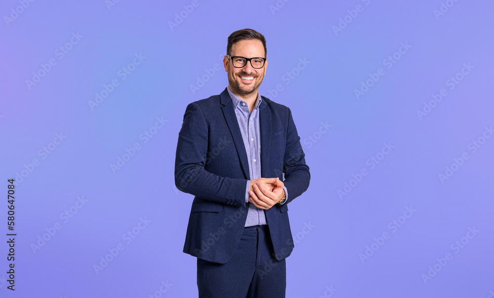Smiling elegant mid adult male manager dressed in blue suit clasping his hands while standing confidently isolated over blue background - obrazy, fototapety, plakaty 