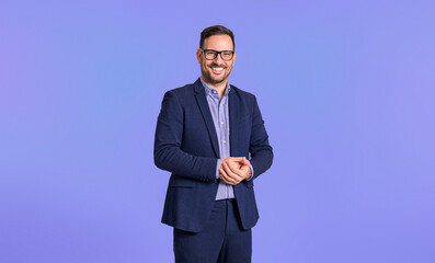 Smiling elegant mid adult male manager dressed in blue suit clasping his hands while standing confidently isolated over blue background