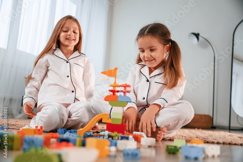 Toys are on the floor. Two little girls are playing and having fun together in domestic room