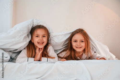 Kids are lying down on the bed. Two little girls are playing and having fun together in domestic room