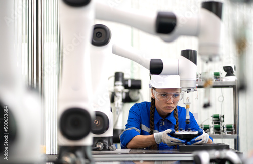 Robotic maintenance engineer working on robot arm connection and control using a remote control. Smart woman in industry 4.0 robotic engineering workshop in an electronic futuristic technology center