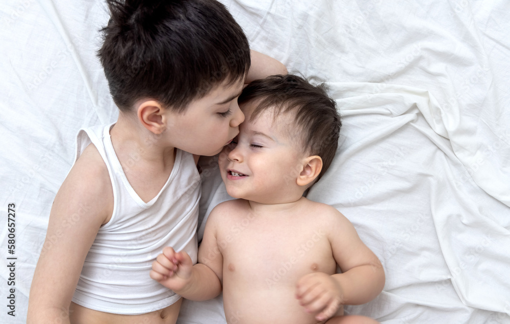 emotional photo with two brothers lying on bed hugging kiss each other cuddling and caresses.big brother kissing little one.different face expression emotion kids child baby boy maternity concept top emotional photo with two brothers lying on bed hugging kiss each other cuddling and caresses.big brother kissing little one.different face expression emotion kids child baby boy maternity concept top