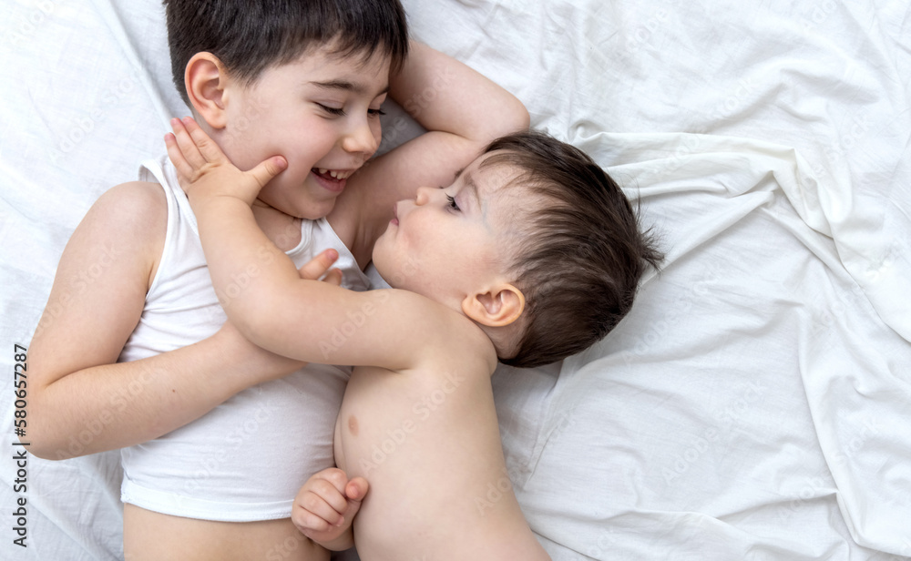 emotional photo with two brothers lying on bed hugging kiss each other cuddling and caresses.big brother kissing little one.different face expression emotion kids child baby boy maternity concept top emotional photo with two brothers lying on bed hugging kiss each other cuddling and caresses.big brother kissing little one.different face expression emotion kids child baby boy maternity concept top