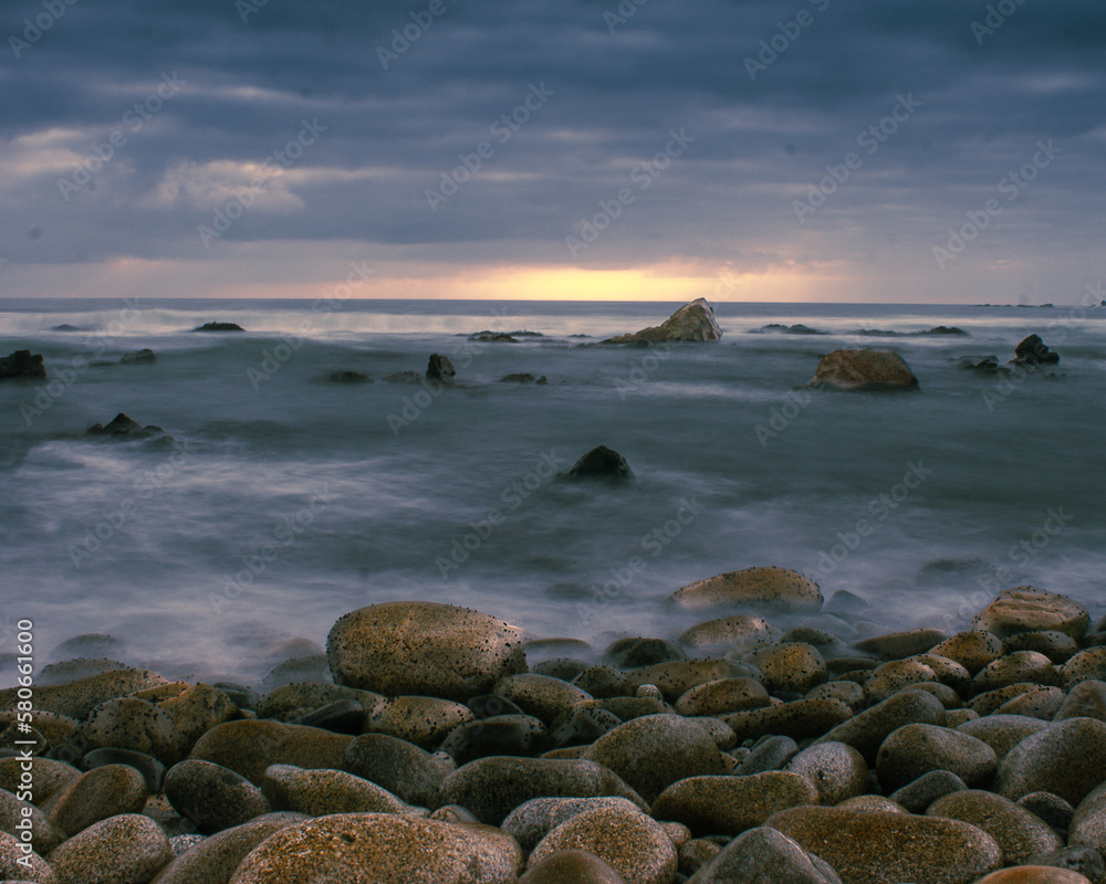 
Long exposure coastal sunset landscape with stones in the foreground, rocks in the middle shot and horizon and clouds in the background