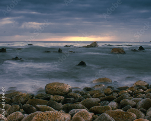  Long exposure coastal sunset landscape with stones in the foreground, rocks in the middle shot and horizon and clouds in the background