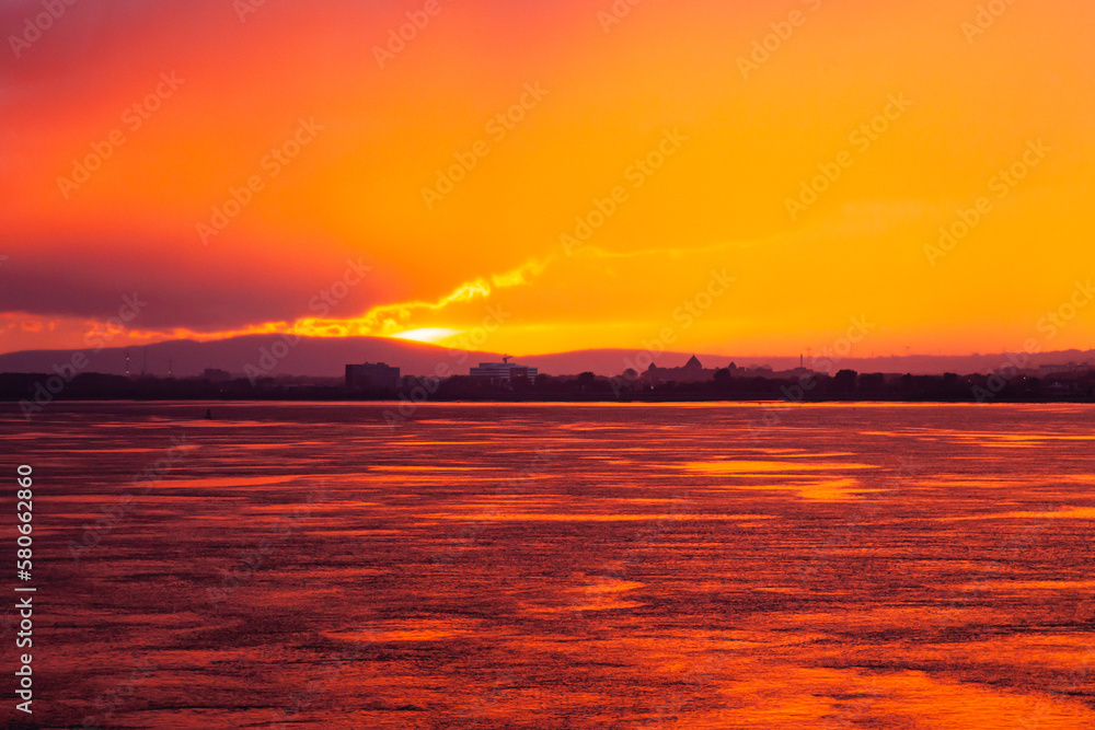 Colorful bright orange sunset in the sea bay at dusk and the city in the distance.