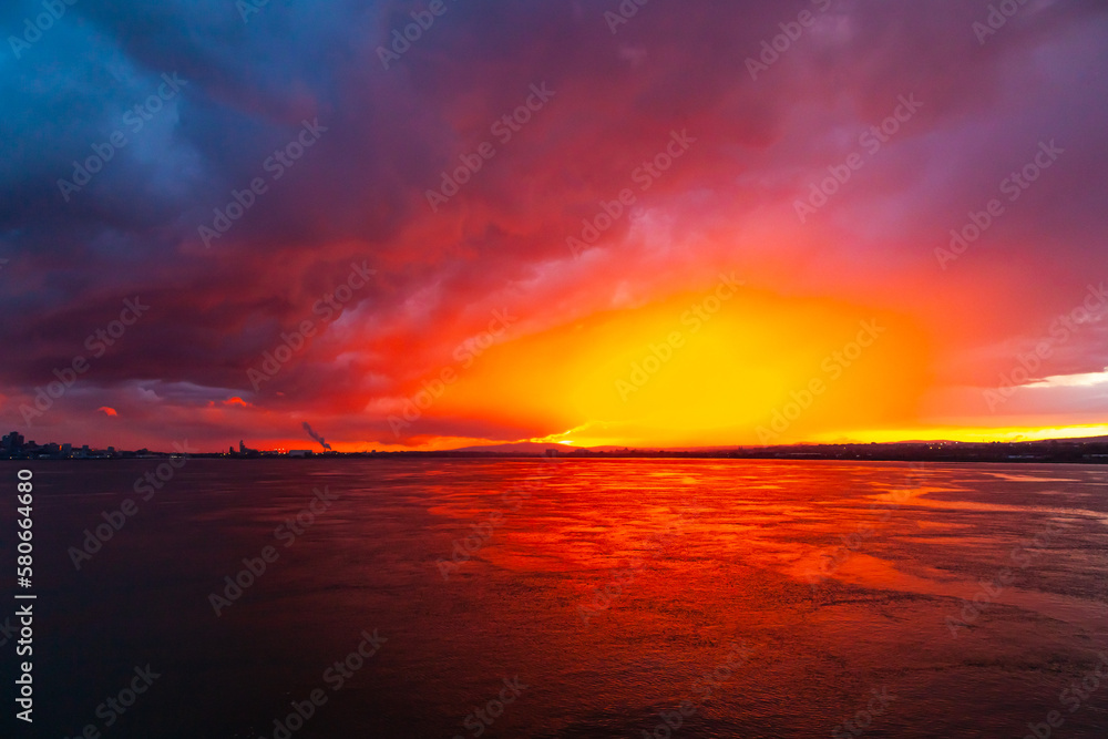 Colorful red and blue sunset in the sea bay at dusk and the city in the distance.
