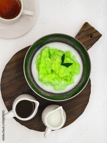 Bubur Sumsum Pandan is Indonesian rice flour porridge 
green colored by pandan leaves  served with palm sugar sauce & coconut milk, garnish with pandan leaf in white bowl. On white background 
