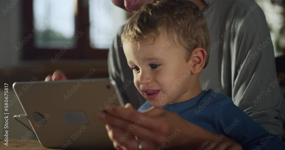 Authentic Shot of Little Boy Using Digital Tablet Computer With his Mother to Have a Video Call with Family While Sitting at Home in the Kitchen. Woman and her Son Waving and Greeting Authentic Shot of Little Boy Using Digital Tablet Computer With his Mother to Have a Video Call with Family While Sitting at Home in the Kitchen. Woman and her Son Waving and Greeting