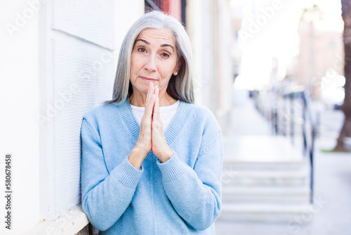 senior retired pretty white hair woman feeling worried, hopeful and religious, praying faithfully with palms pressed, begging forgiveness