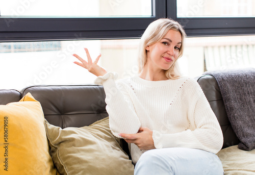 young pretty woman smiling proudly and confidently, feeling happy and satisfied and showing a concept on copy space sitting on a couch