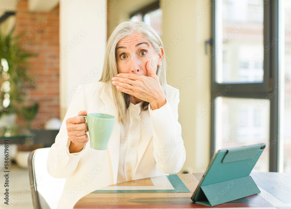 senior pretty woman covering mouth with a hand and shocked or surprised expression with a touch screen senior pretty woman covering mouth with a hand and shocked or surprised expression with a touch screen
