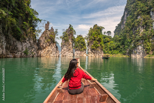 Boat riding through mountain lake view with woman tourist and tropical forest at Sam Klur mountain Khaosok National Park, Surat Thani Thailand nature landscape © Noppasinw