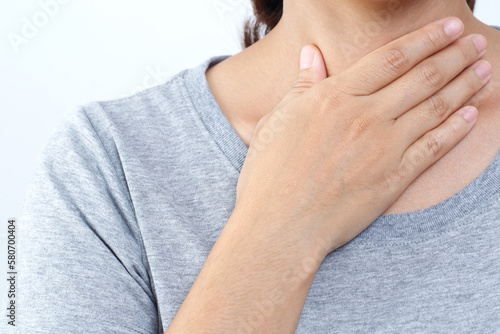  sore throat pain. Closeup of young woman sick holding her inflamed throat using hands to touch the ill neck in blue shirt on gray background. Medical and healthcare concept. Focus red on to show pain