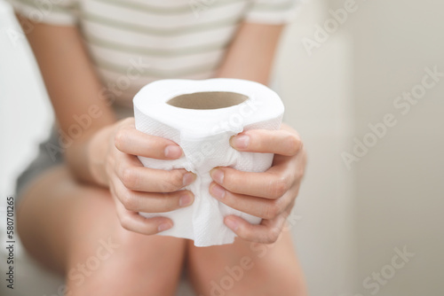 portrait of a woman suffers from diarrhea his stomach painful. ache and problem. hand hold tissue paper roll in front of toilet bowl. constipation in bathroom. Hygiene, health care concept. photo