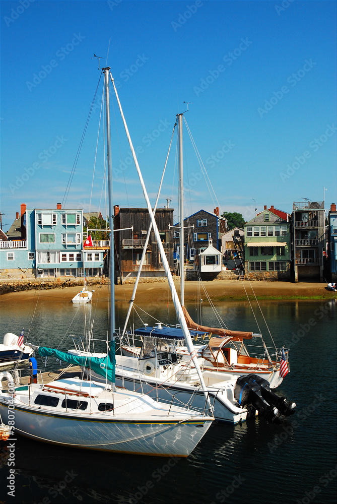 Sailboats and other recreational boats and ships are moored in a small marina along the New England Coast