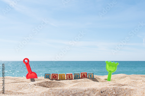 Holiday letters on cubes in the sand and ocean in the background. Copy space. Vacations background. Kids sand toys.