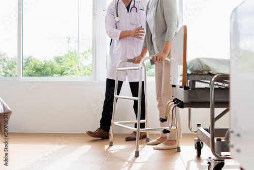 Caucasian male doctor helping female patient try to walk with walker. Doctor is examining the patient in the hospital.