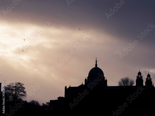 Silhouette of Galway Cathedral building against dark dramatic sky with birds flying high in the air. Famous town landmark and point of tourist attraction. Catholic faith in Ireland.