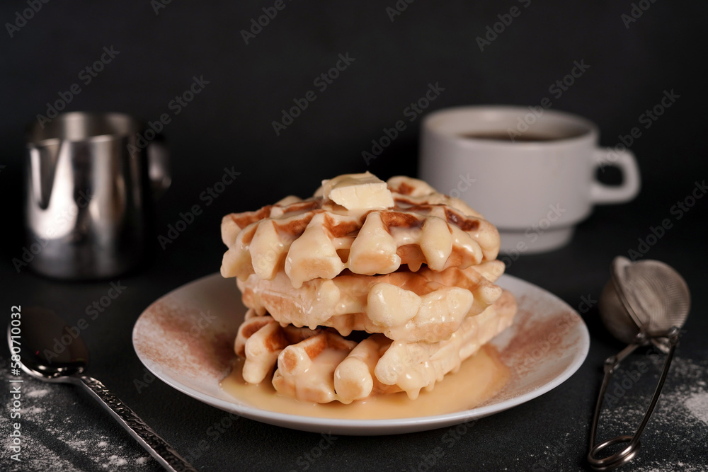 Homemade of tasty Belgian Waffles Plate, Caramel Sauce, Coffee Cup, Milk on a Black concrete Background Homemade of tasty Belgian Waffles Plate, Caramel Sauce, Coffee Cup, Milk on a Black concrete Background