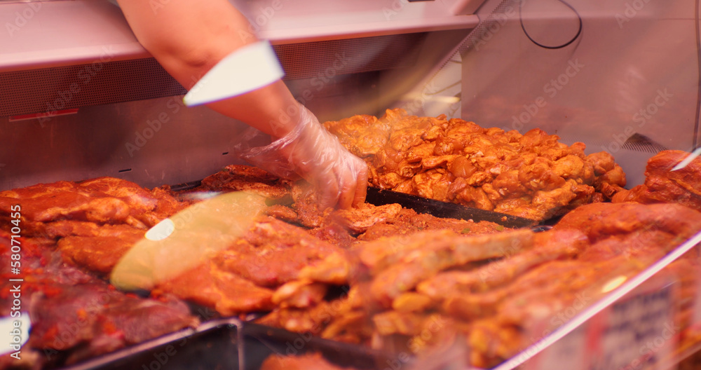 Seller chooses two pieces of meat in a shop window close up. Female hands picking seasoed meat to weight it up. Food industry. Seller chooses two pieces of meat in a shop window close up. Female hands picking seasoed meat to weight it up. Food industry.