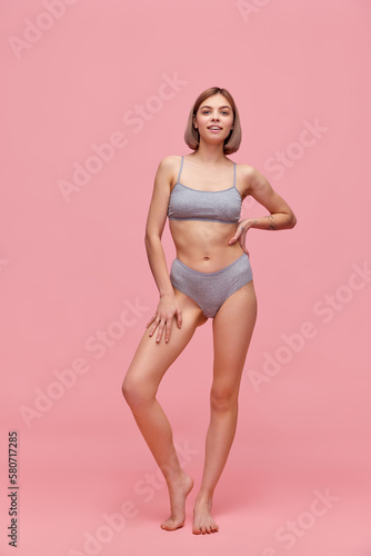 Portrait of young thin sportive woman in grey cotton inner wear posing over pink background. Concept of natural beauty, body and skin care, healthy eating