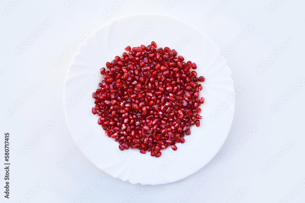 Pomegranate seeds, or kernels on the plate. Juicy pomegranate arils showing beautiful shades of red against white background, top view. Bright colors of ripe tasty fruit, healthy food concept.