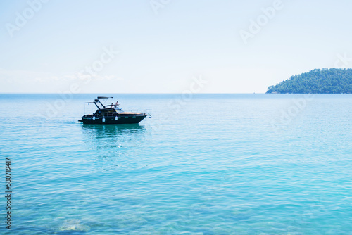 A tranquil scene of a nautical vessel on calm, clear blue waters against an expansive horizon under a beautiful sunny sky.