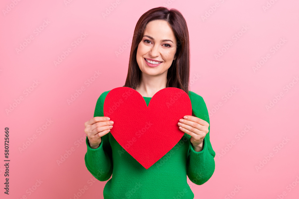 Photo of positive adorable lady dressed green pullover holding red big heart isolated pink color background Photo of positive adorable lady dressed green pullover holding red big heart isolated pink color background