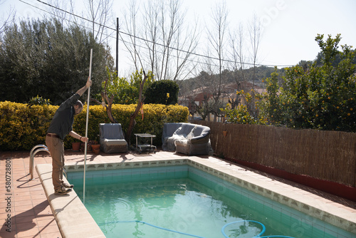 boy in charge of pool maintenance running the manual pool cleaner and preparing the water for the end of winter