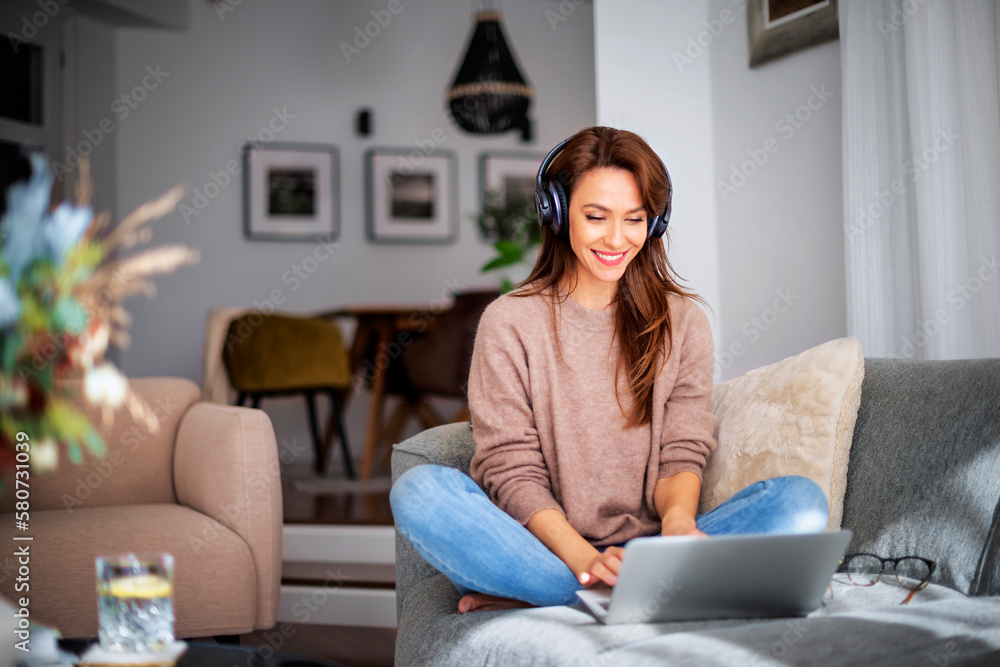 Cheerful woman using headphone and laptop and relaxing at home Cheerful woman using headphone and laptop and relaxing at home