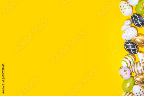 Bright Easter greeting card background. Trendy colored black, golden, stripe painted Easter eggs with white bunny rabbits decor, tulip flower on high-colored yellow background, flat lay copy space