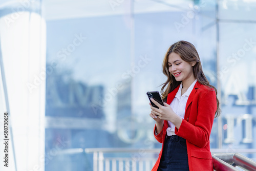 Outdoor portrait of elegant smiling woman in red dress holding smartphone. Cheerful woman using mobile phone to chat and text with friends.