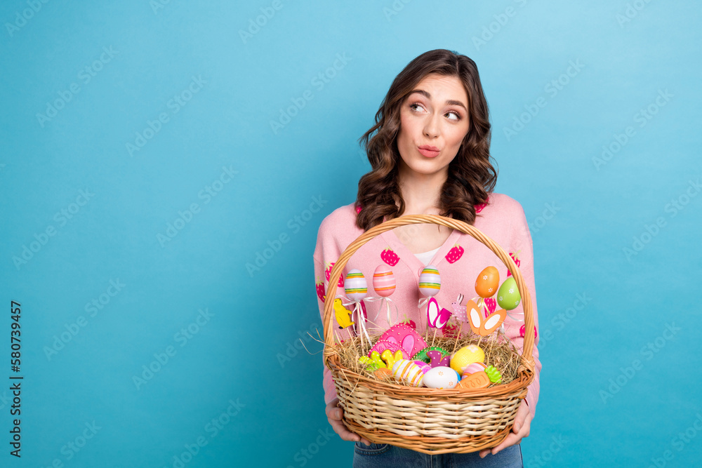 Photo of adorable dreamy woman wear pink cardigan looking empty space rising easter sweets basket isolated blue color background Photo of adorable dreamy woman wear pink cardigan looking empty space rising easter sweets basket isolated blue color background